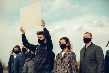 Koronavirüs karşıtı protestoları ve koronavirüs ve insan haklarıyla ilgili karantina toplantısını protesto etmek için posterlerle gelen maskeli bir grup insan. Kopyalama alanı