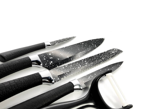 Set of professional black knives and peeler isolated on a white background. Composition of the chef knife, bread knife, utility knife, paring knife and ceramic peeler.