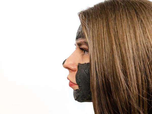 Woman with clay or mud mask on her face on a white background. Face with clay mask in profile. Black clay face mask.