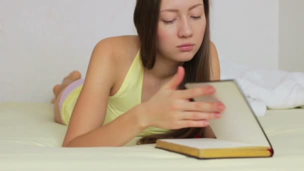 Schönes junges Mädchen liest ein Buch, das auf dem Bett liegt — Stockvideo