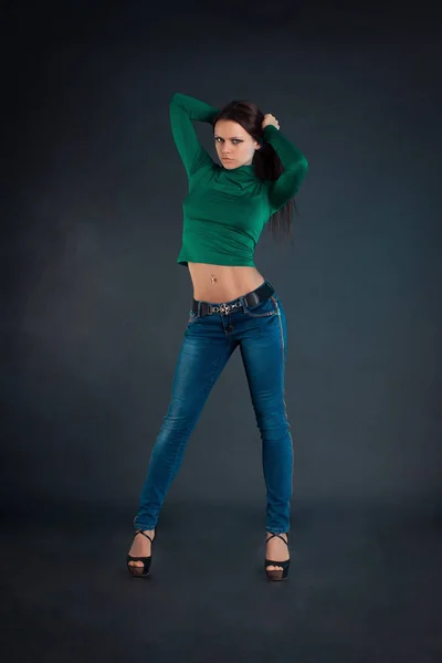Krásná mladá dívka v modrých džínách na tmavém pozadí — Stock fotografie