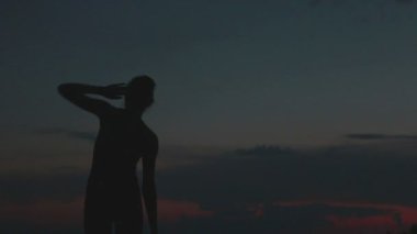 Kız bir dağın tepesinde gün batımında yoga yapar