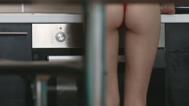 Сексуальная женщина в обтягивающем платье флиртует на кухне, показывая задницу — стоковое видео