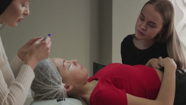 Beautiful young girl admires eyelashes, which her build-up in a beauty salon — Stock Video