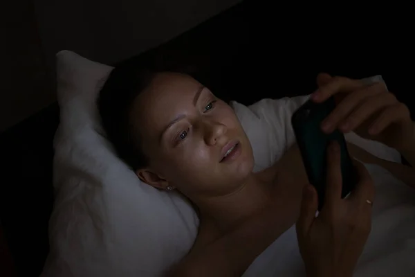 Young Woman Lying In Bed And Using Smartphone