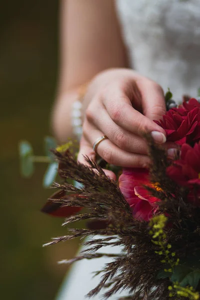 Mariée tenant bouquet avec des fleurs vineuses en composition avec des herbes vertes et brunes — Photo