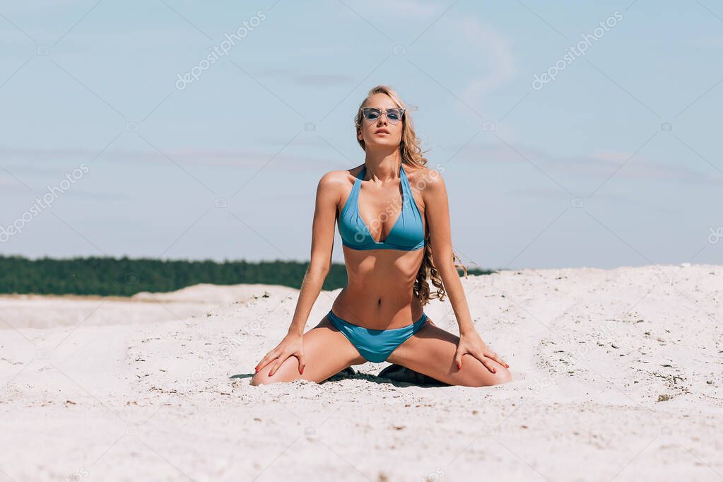 Seductive woman in stylish swimsuit kneeling in sand