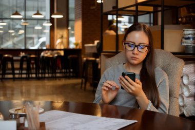 Kafede akıllı telefon kullanan genç bir kadın.