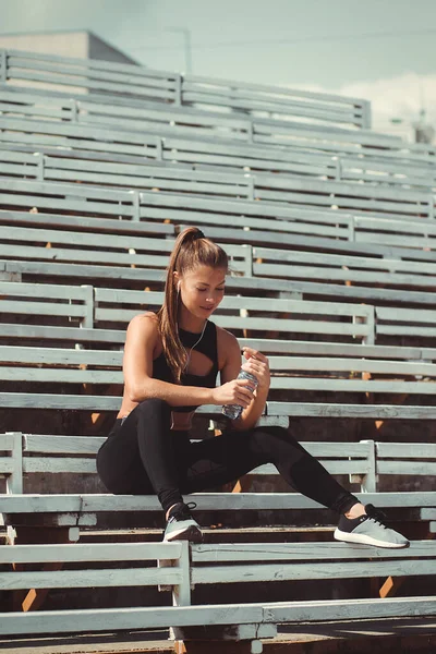 Mujer cansada en auriculares descansando y bebiendo agua en la tribuna — Foto de Stock