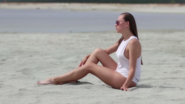 Languid vrouw zittend cross-legged op zand aanraken van de huid — Stockvideo