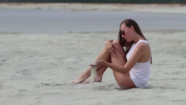 Νωθρή γυναίκα κάθεται με σταυρωμένα πόδια στην άμμο αγγίζοντας το δέρμα — Αρχείο Βίντεο
