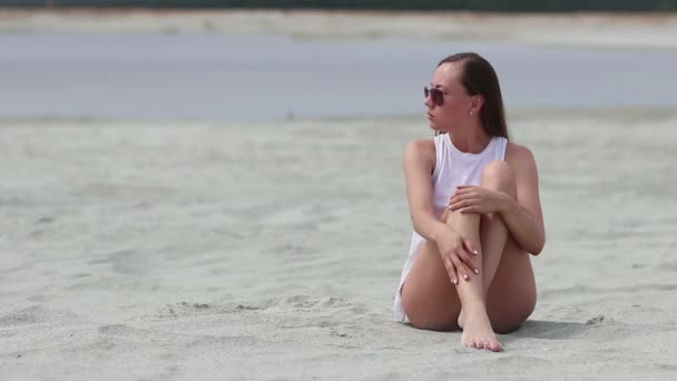 Schwache Frau sitzt im Schneidersitz auf Sand und berührt die Haut — Stockvideo
