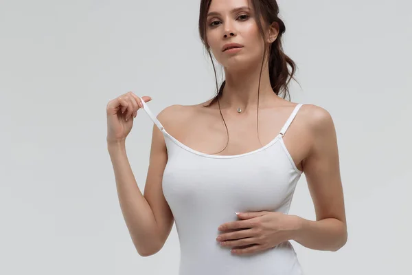 Mujer atractiva tirando de la correa de camiseta blanca y mirando a la cámara — Foto de Stock