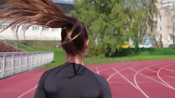 Mujer delgada corriendo en pista de carreras bajo el sol — Vídeo de stock