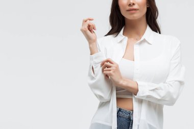 Beyaz gömlekli ve kot pantolonlu şık bir kadın kameraya özgüvenle bakıyor.