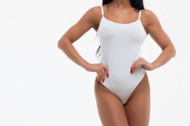 Mahsul baştan çıkarıcı genç bir kadın mayosunu çıkarıyor. Stüdyoda beyaz arka planda seks pozu veriyor.