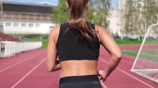Mujer delgada corriendo en pista de carreras bajo el sol — Vídeos de Stock