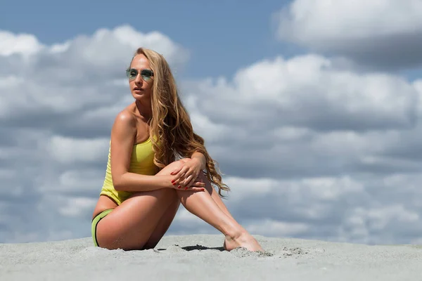 瘦长发性感的女人与太阳眼镜在沙滩的阴天背景上摆出诱人的活力姿势 — 图库照片