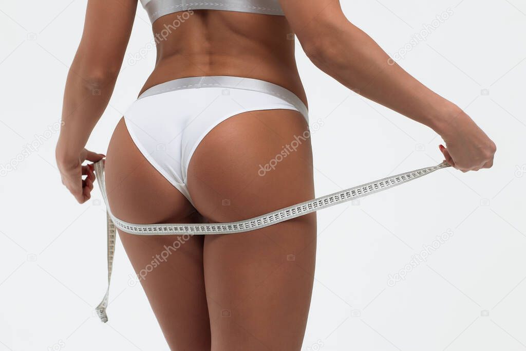 Back view of crop alluring young female in white panties measuring body parts of roulette in studio on white background