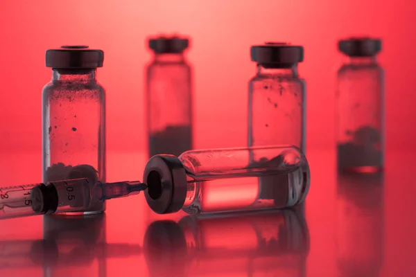 Kırmızı arka planda plastik tek kullanımlık şırınga ile birlikte antibiyotik enjeksiyon şişeleri.