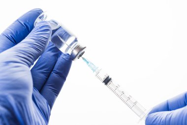 Doktor şırıngayı dolduruyor. Ellerinde şeffaf antibiyotik ya da mavi lateks eldivenli aşı olan cam şişe..