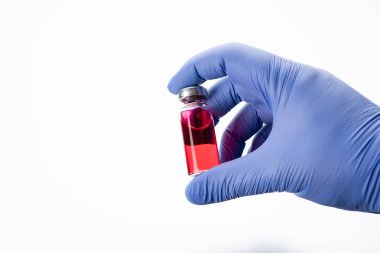 Bir doktorun elinde cam bir ilaç şişesi. Kırmızı antibiyotik ya da aşı içeren bir şişede beyaz arka planda silikon eldivenler bulunur..