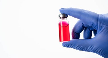 Bir doktorun elinde cam bir ilaç şişesi. Kırmızı antibiyotik ya da aşı içeren bir şişede beyaz arka planda silikon eldivenler bulunur..