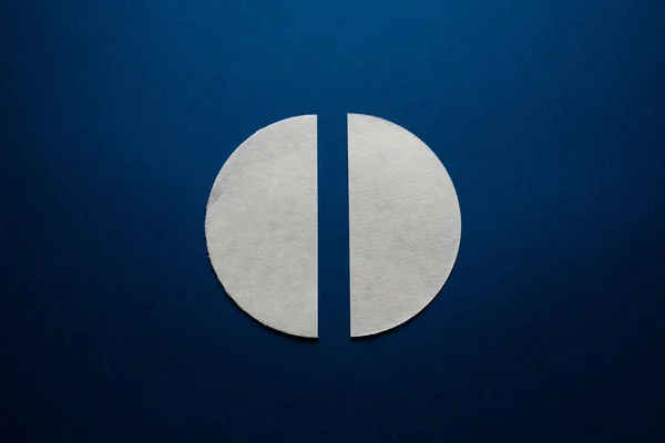 A gray paper circle is cut in half. Two halves of one whole on dark blue.
