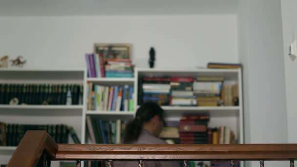 Bookshelve bir kitap toplama ve odakta geliyor rahat orta yaşlı adam — Stok video
