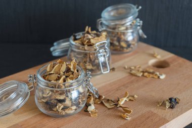 Üç koruma çeşitli mantar cam kase ayakta ahşap koltukta veya karanlık yapılandırılmış arka planda çok yumuşak odak masada dilimlenmiş ve kurutulmuş. Doğranmış kurutulmuş mantar.