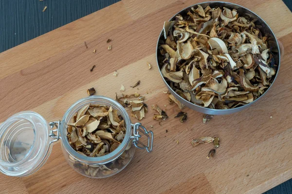 Top or flat view of sliced, chopped and dried vairous mushrooms in preserving glass and silver bowl on wooden desk with dark background.