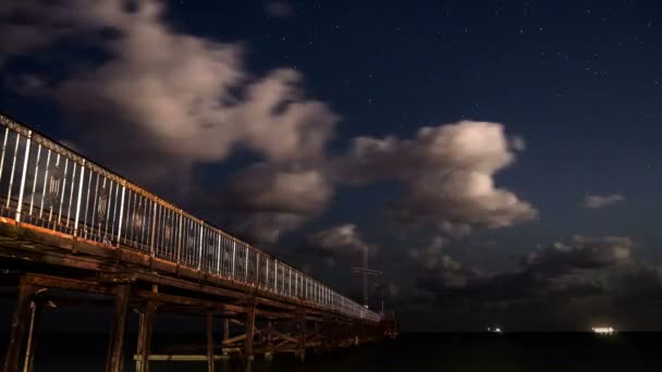 Estrellas y nubes moviéndose sobre el muelle. 4K time-lapse video de la noche llena de estrellas con nubes en la playa en Bulgaria con olas de mar . — Vídeos de Stock