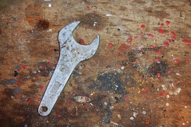 Eski ahşap bir masada üzerinde boya izleri olan bir İngiliz anahtarı.                               