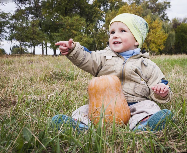 Мальчик с большой желтой тыквой в руках сидит на траве — стоковое фото