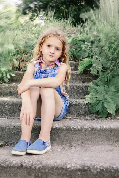 Little girl with blond hair sitting on the steps — Stock Photo, Image