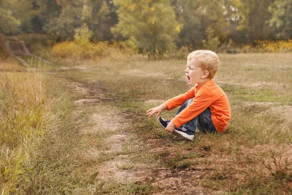 Мальчик в синих джинсах горько плачет, сидит на земле — стоковое фото