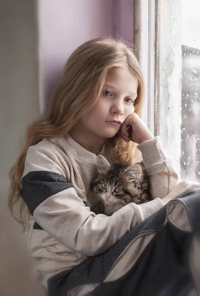 Cute little girl sitting by the window with fluffy cat — Stock Photo, Image