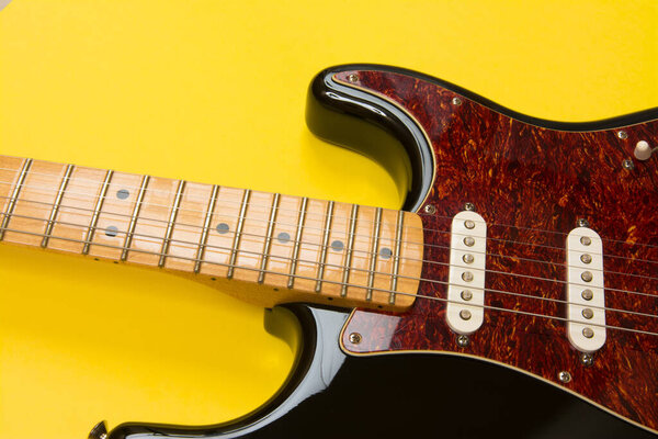 Close-up of electric guitar on yellow background, with copy space