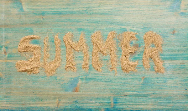 Sand on blue planked wood with the word Summer. Background with copy space. Top view