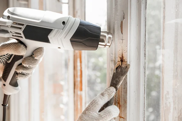 Master removes old paint from window with heat gun and scraper. Closeup. — Stock Photo, Image