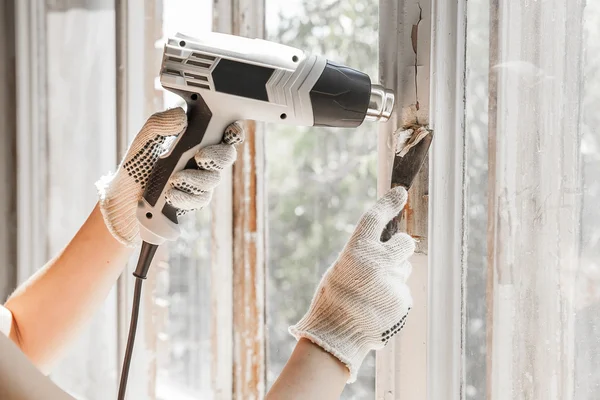 Master elimina la pintura vieja de la ventana con pistola de calor y rascador. Primer plano. Imagen De Stock