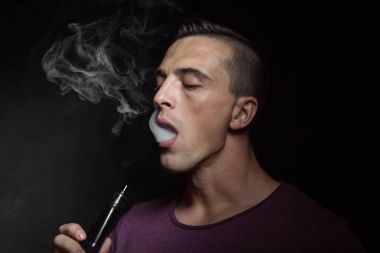 Man on black background vaping and releasing a cloud.  clipart