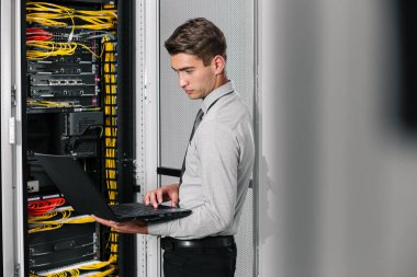 Süper bilgisayarla çalışma sunucu odası laptop ayakta tutan modern genç adam portresi