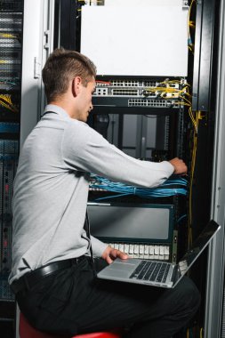 Young man is standing next to the racks with computer equipment clipart