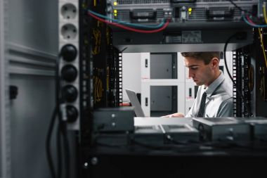 Süper bilgisayarla çalışma sunucu odası laptop ayakta tutan modern genç adam portresi