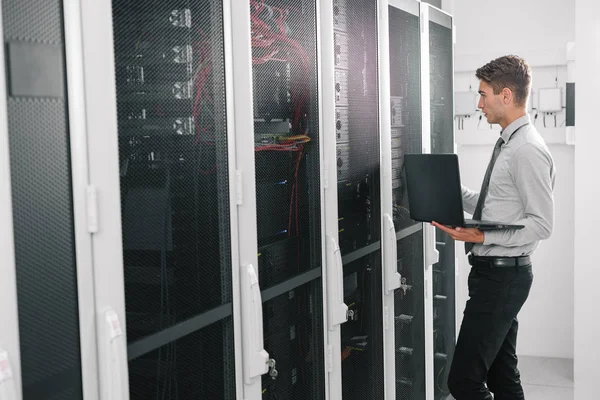 手持笔记本电脑的现代年轻人肖像站在服务器机房使用超级计算机 — 图库照片