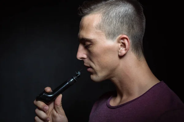 Man on black background vaping and releasing a cloud.