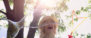 güzel genç esmer kız güneşli parkta sabun köpüğü esiyor.