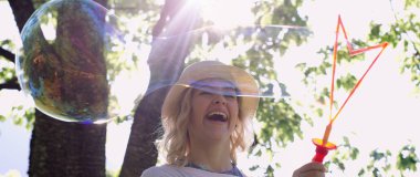 güzel genç esmer kız güneşli parkta sabun köpüğü esiyor.