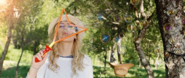 güzel genç esmer kız güneşli parkta sabun köpüğü üfleme.